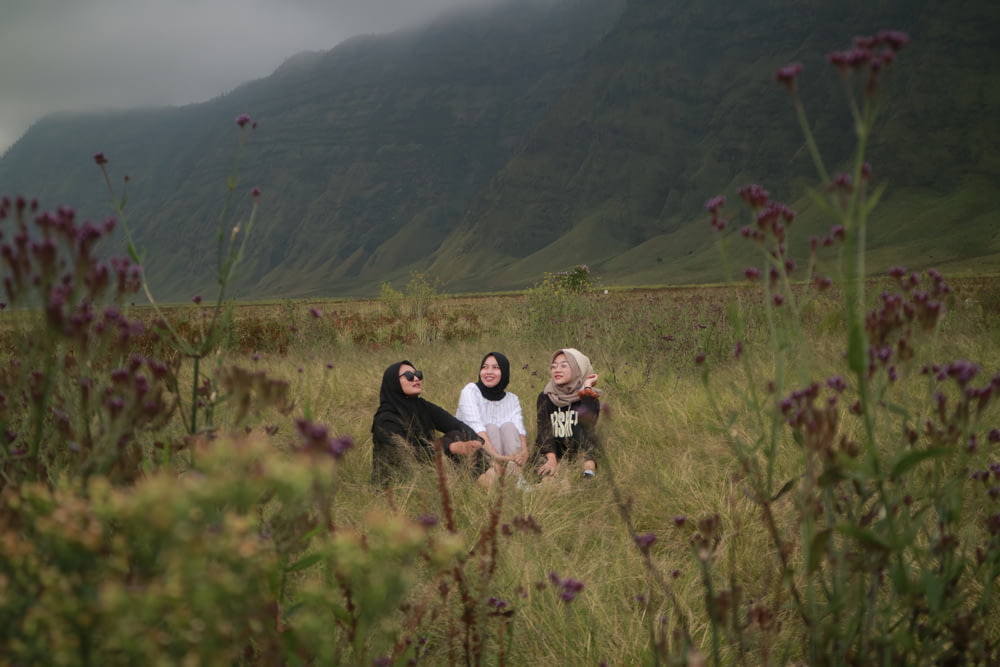 three women sitting in a field with mountains in the background
