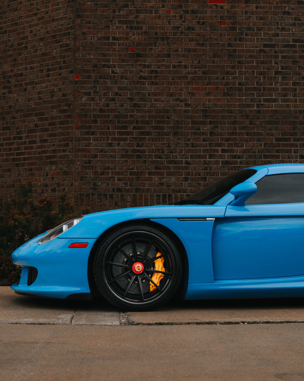 a blue sports car parked in front of a brick wall