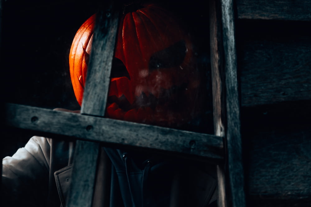 a person wearing a scary pumpkin mask in a window