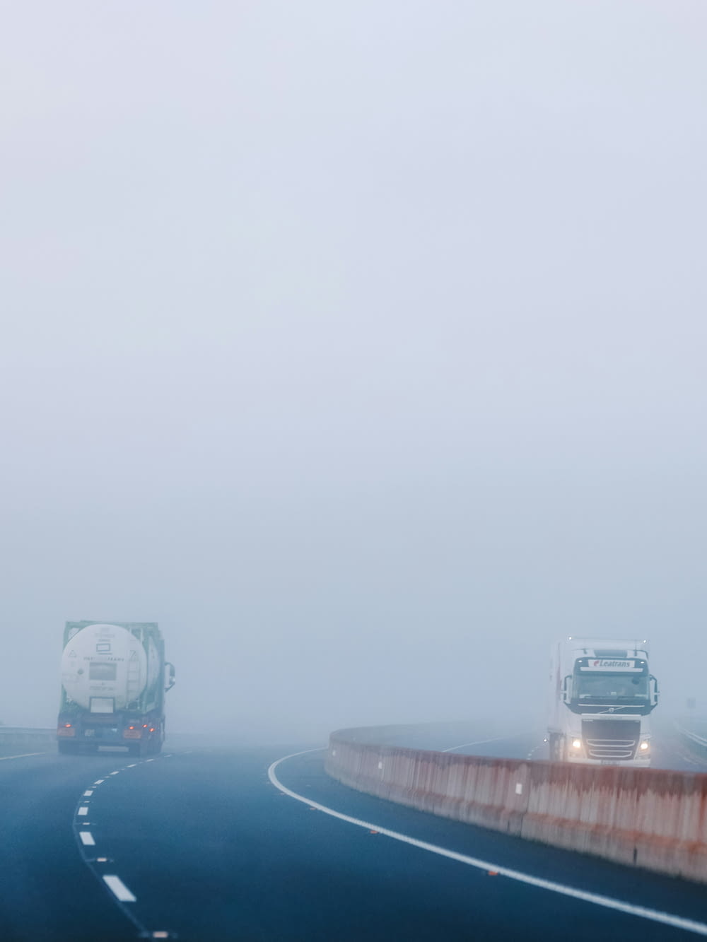 a couple of trucks driving down a foggy road