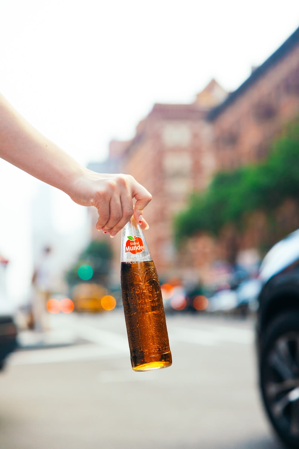 a person holding a bottle of beer on a city street
