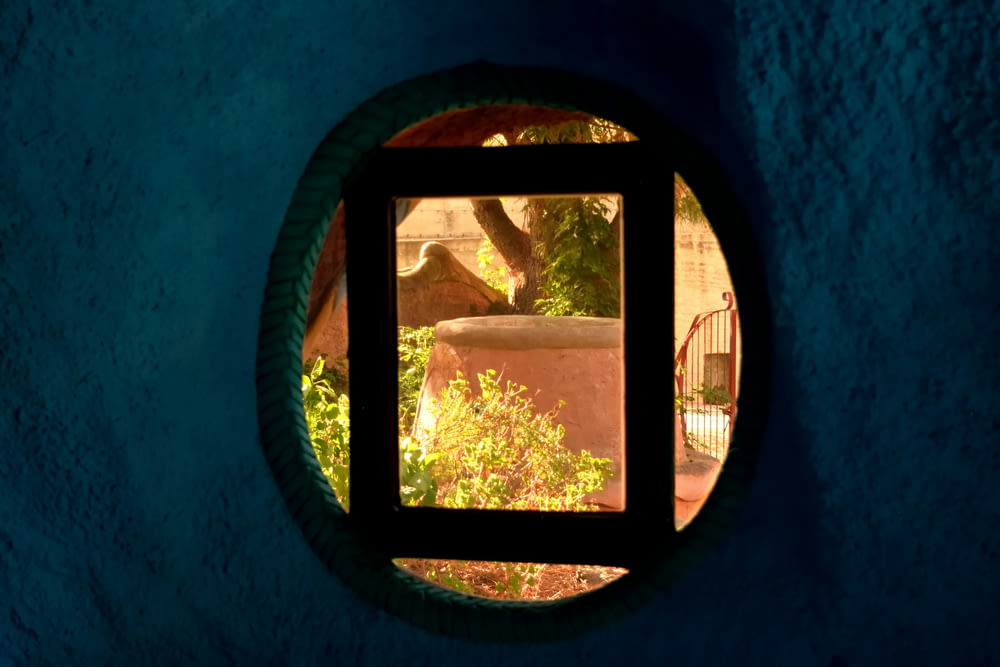 a round window in a blue wall with a view of a garden