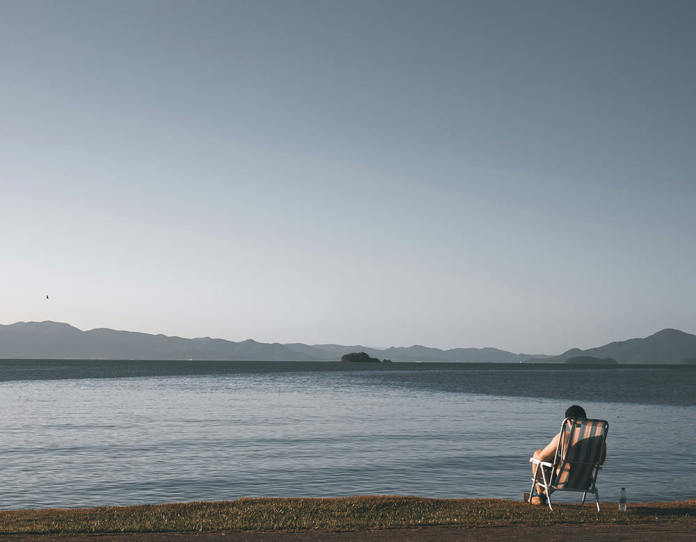 uma pessoa sentada em uma cadeira na margem de um lago