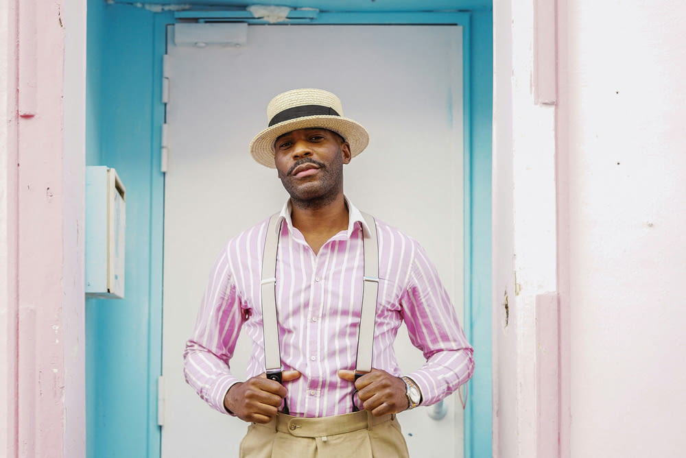 a man wearing a hat and suspenders standing in a doorway