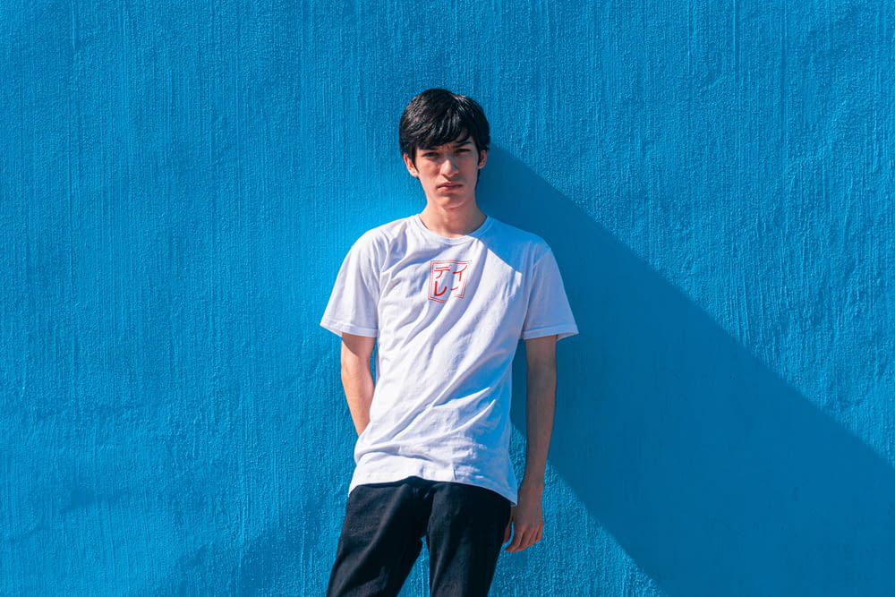 a young man leaning against a blue wall