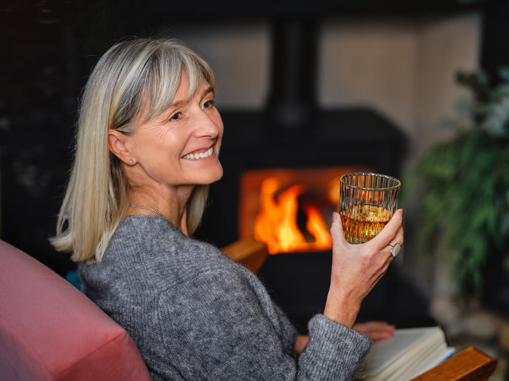 a woman holding a glass of wine in front of a fireplace