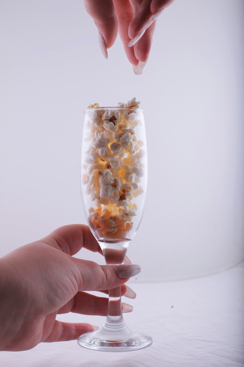 a hand reaching for a wine glass filled with popcorn