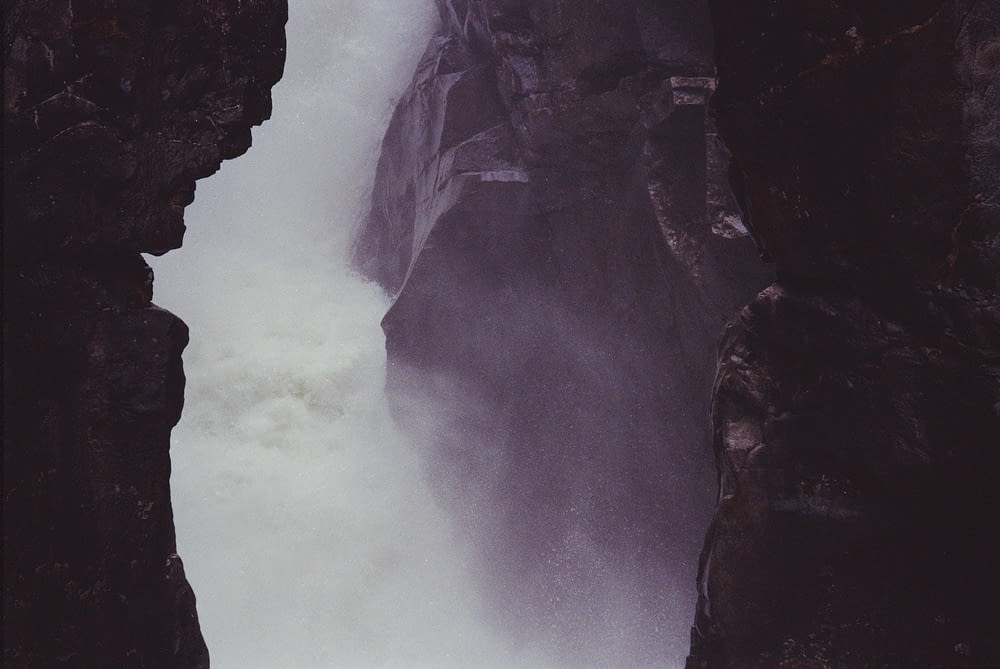 a man standing on top of a cliff next to a waterfall