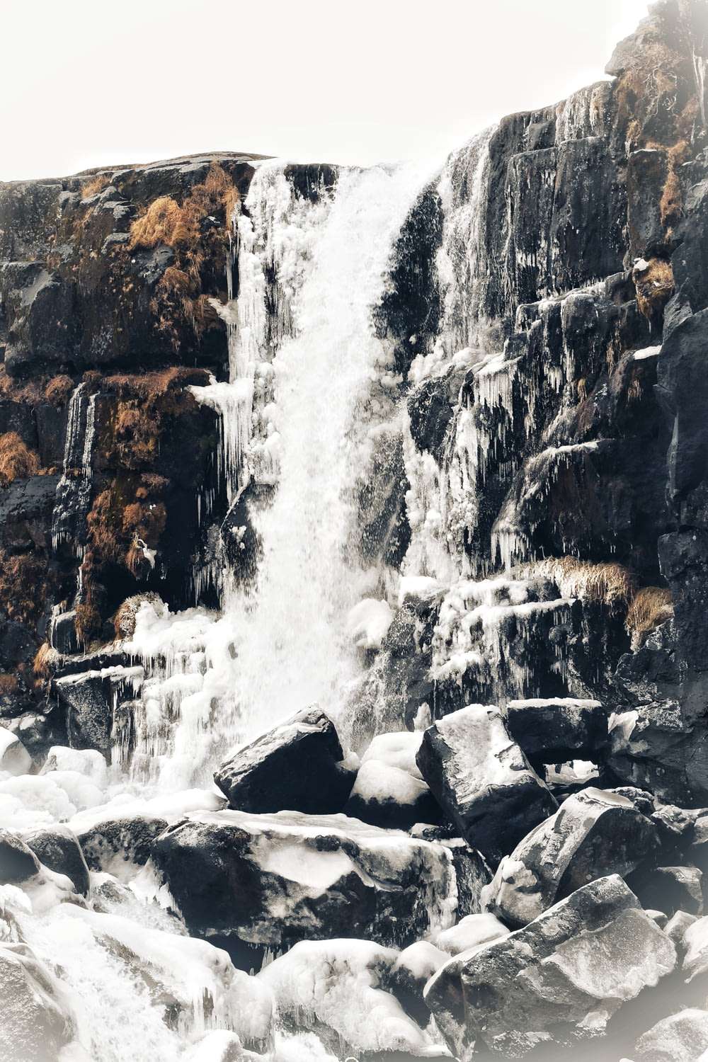 a waterfall with snow on the rocks and ice on the ground
