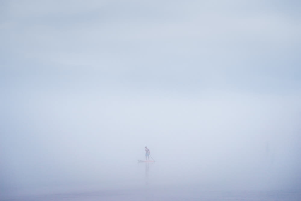 a person standing on a surfboard in the fog