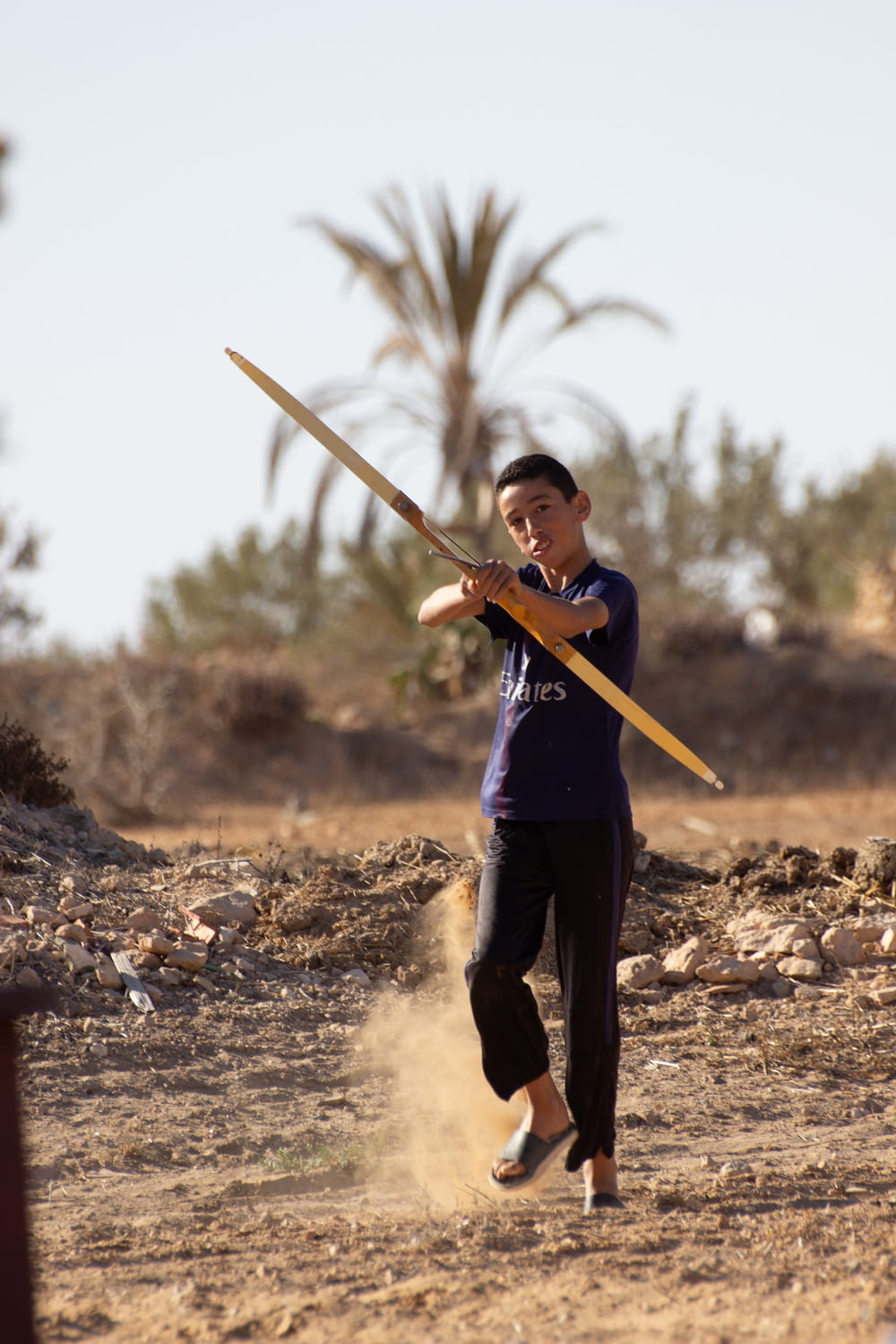 a man holding a large wooden stick on top of a dirt field