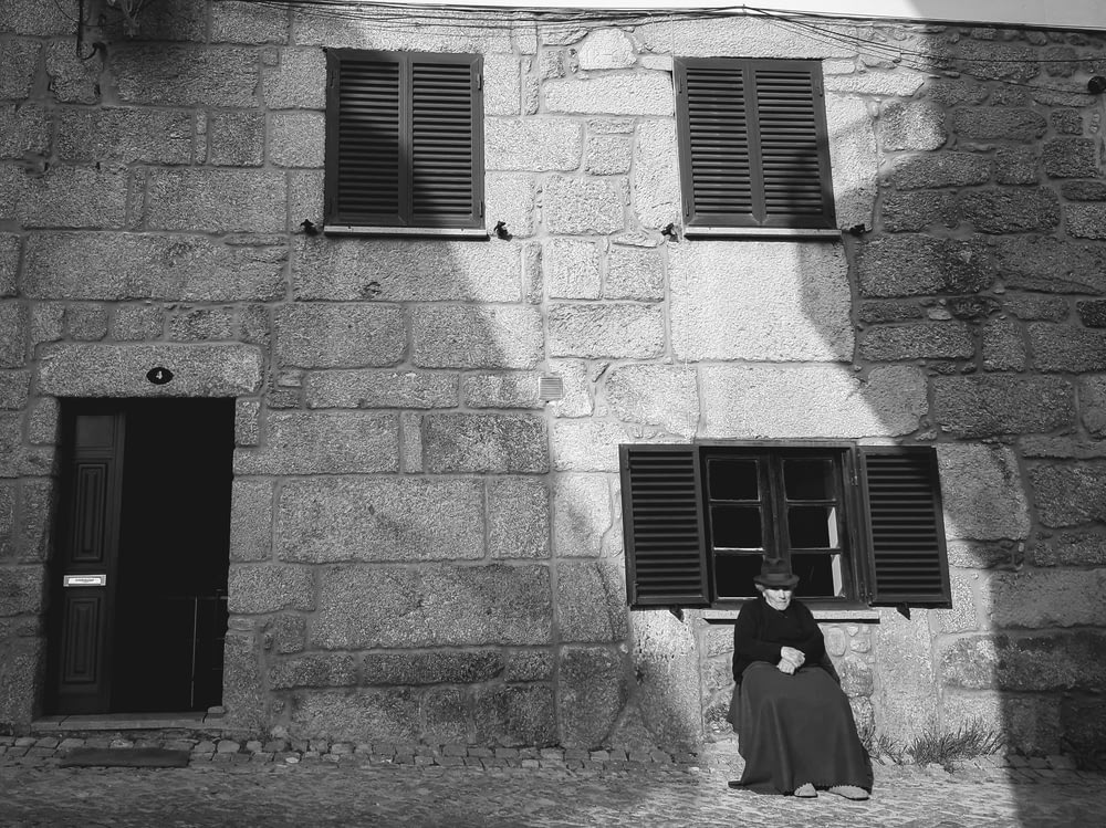 a black and white photo of a woman sitting in front of a building