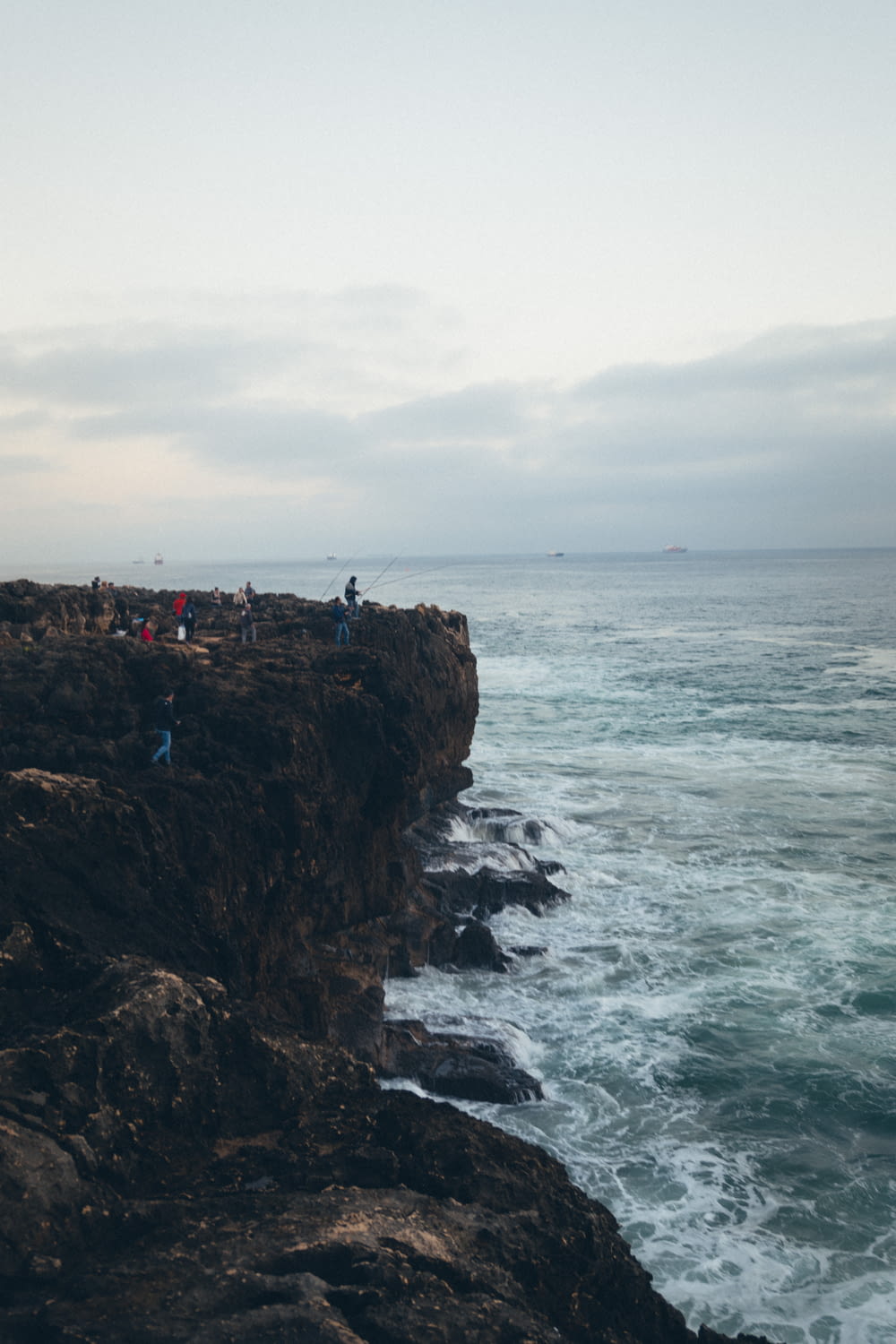a group of people standing on top of a cliff next to the ocean