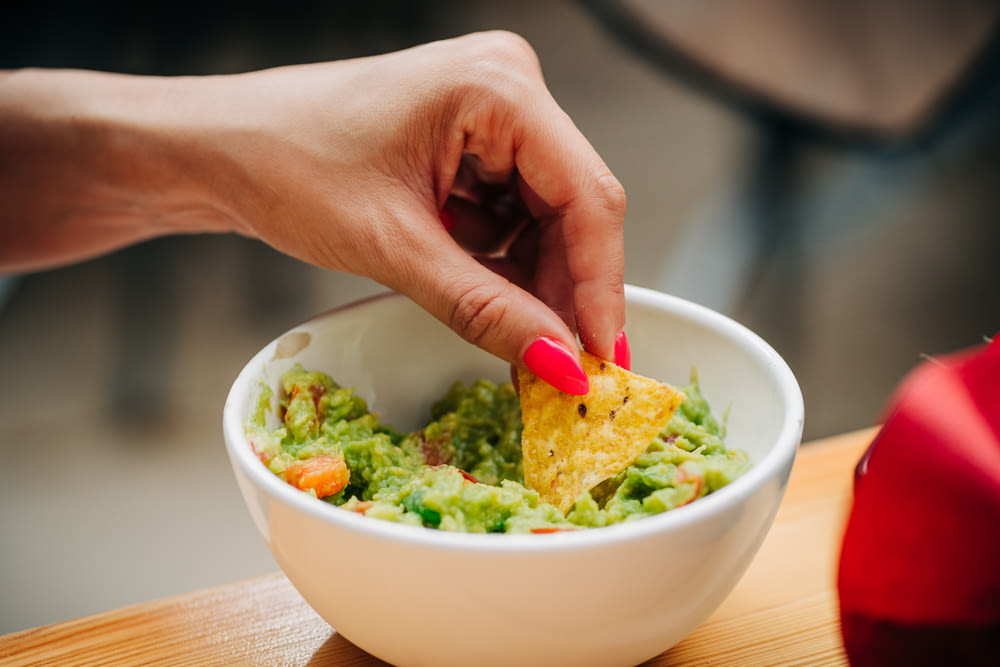 a person dipping a tortilla into a bowl of guacamole