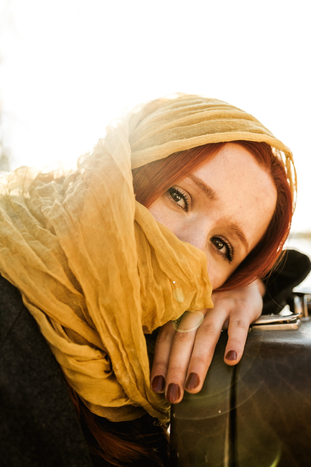 a woman with a yellow scarf on her head leaning against a suitcase