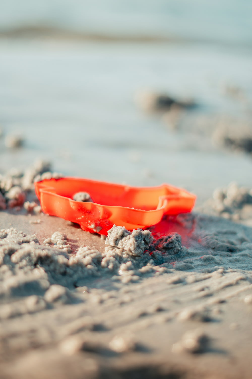 an orange plastic bowl sitting on top of a sandy beach