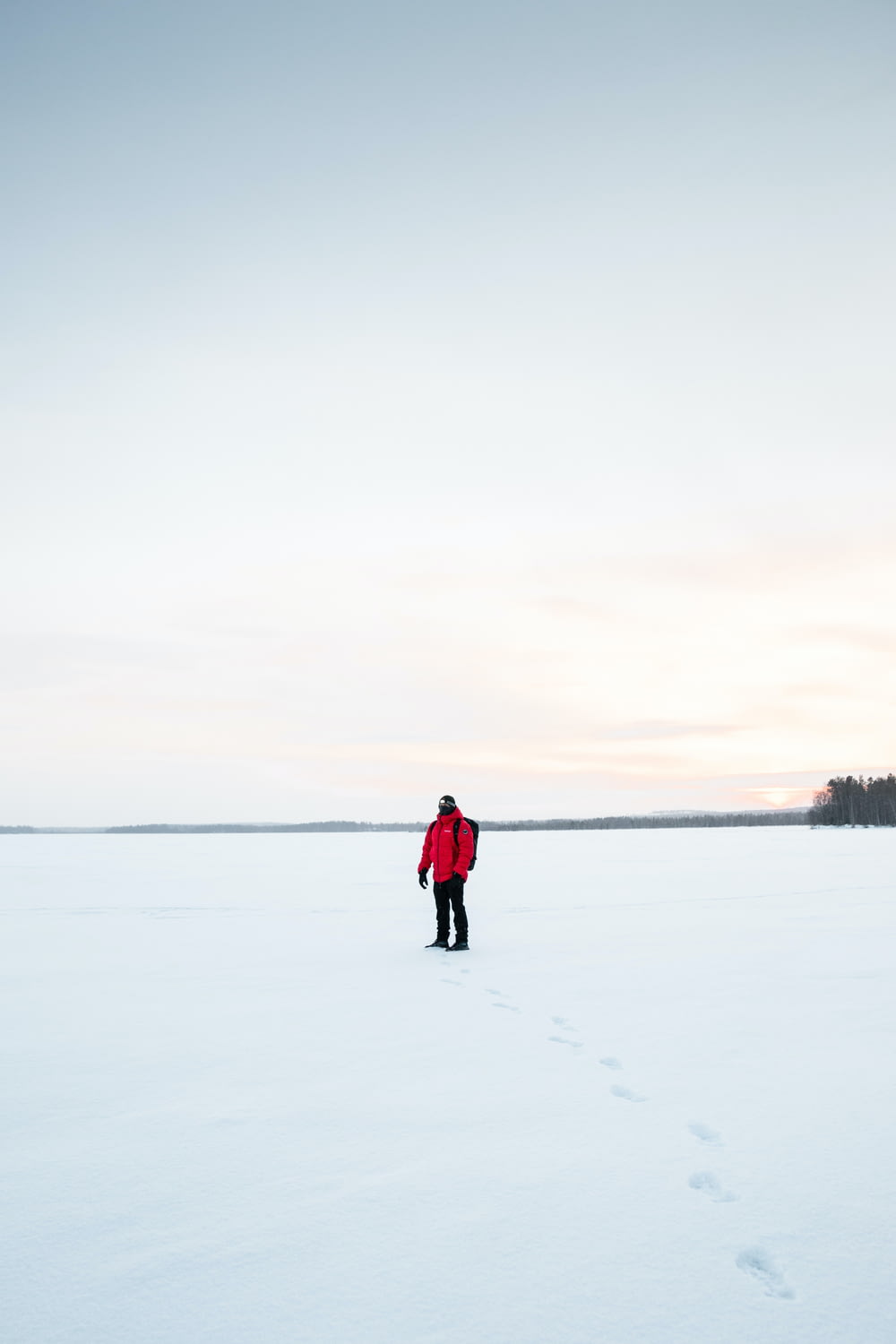 a man in a red jacket walking across a snow covered field