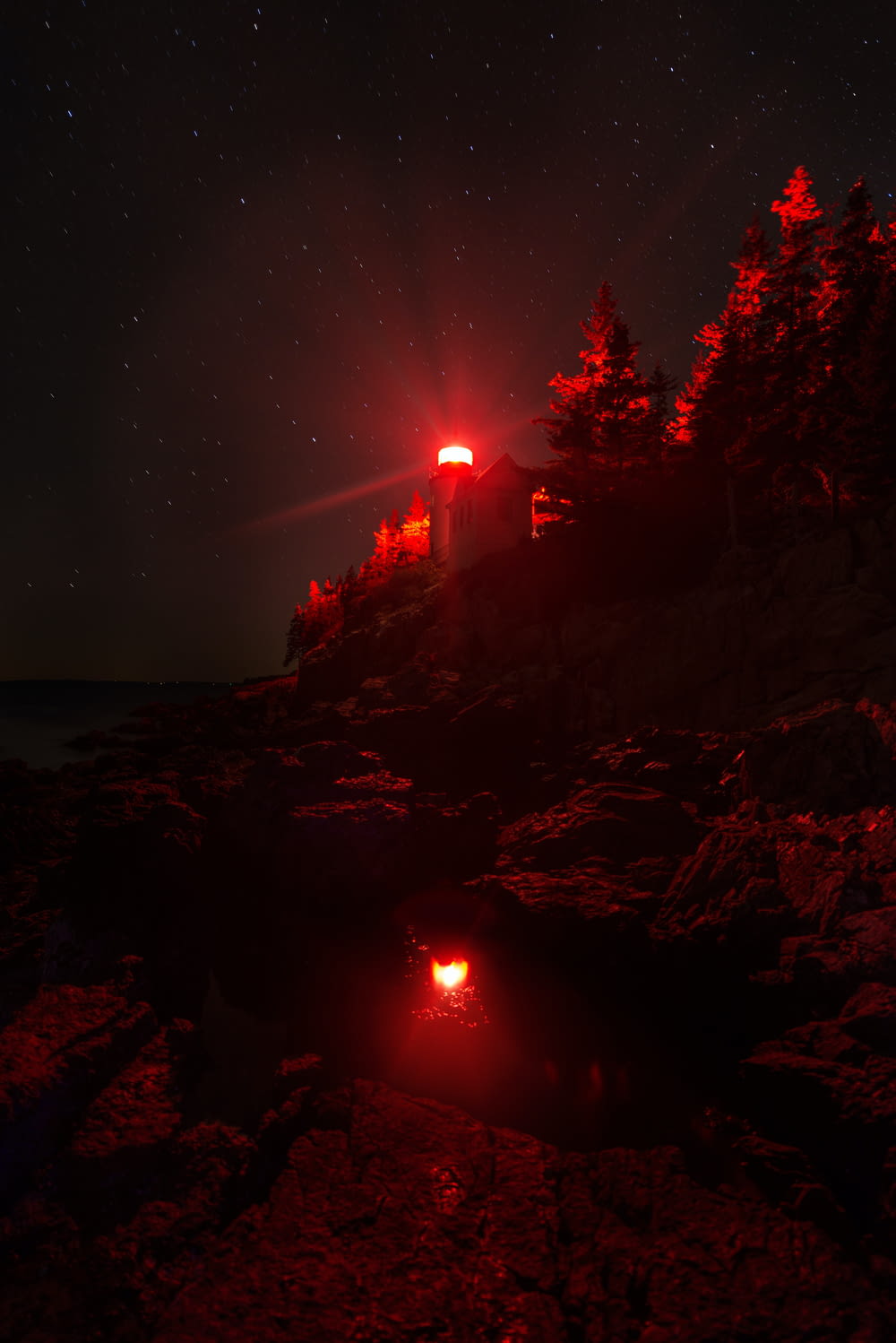 a red light shines on a house on a rocky shore