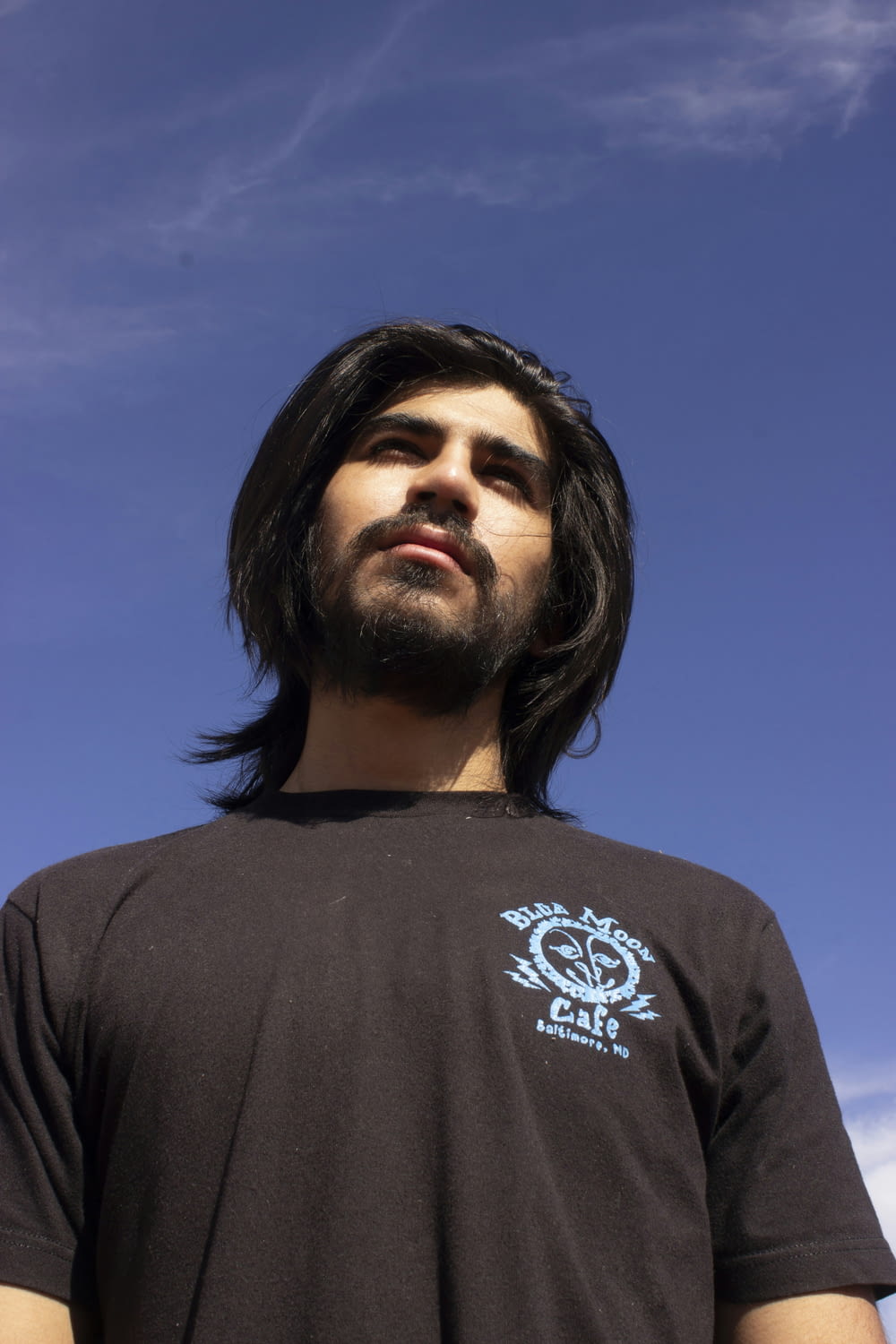 a man with long hair and a beard standing in front of a blue sky