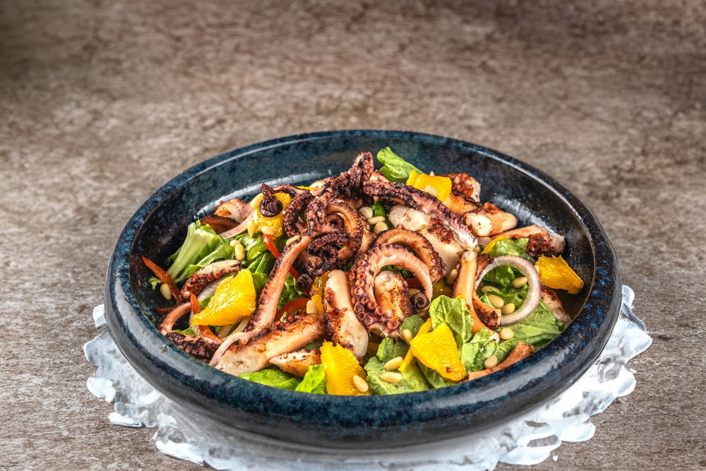 a blue bowl filled with a salad covered in octopus