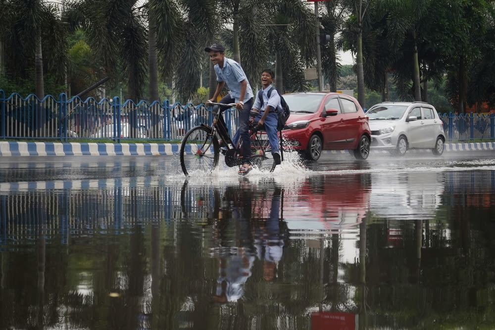 a couple of men riding bikes through a flooded street