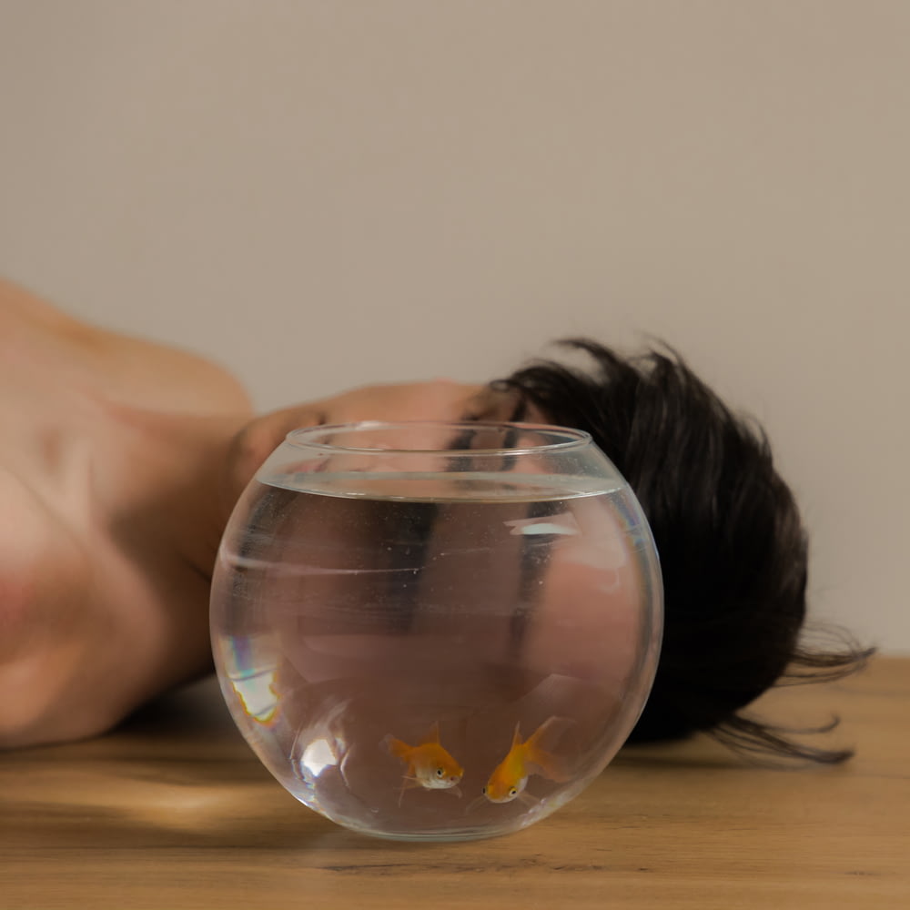 a person laying on a table next to a fish bowl
