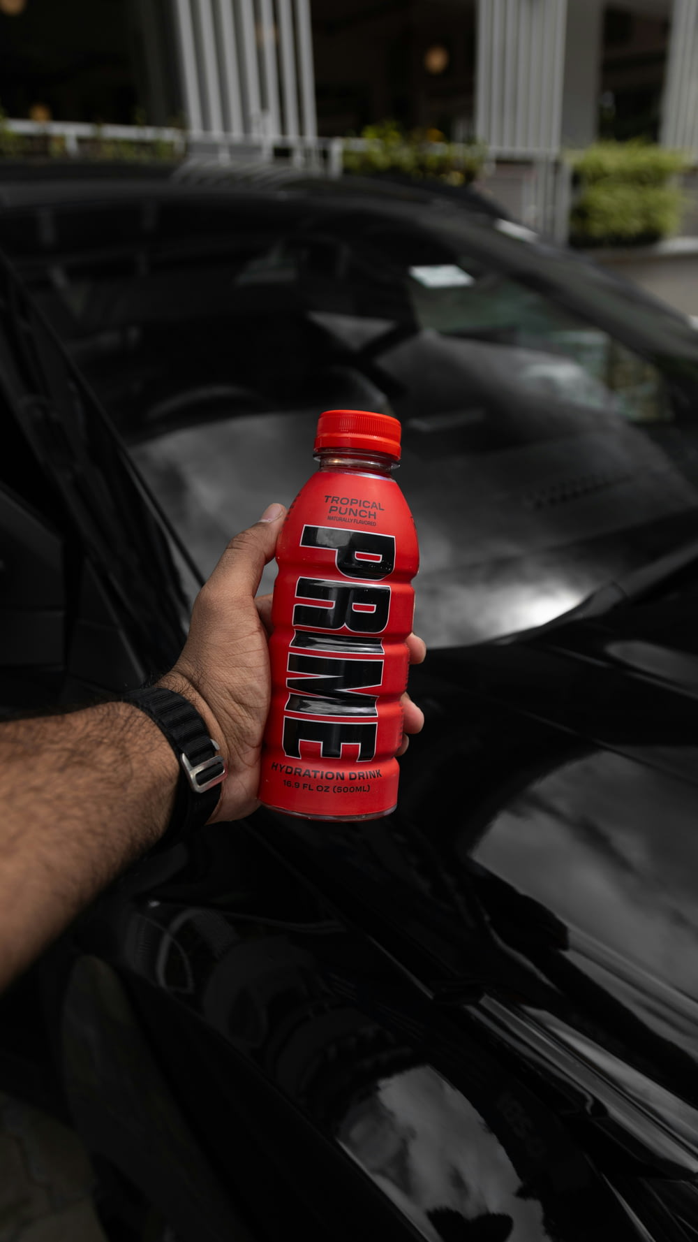a hand holding a bottle of protein drink in front of a black car