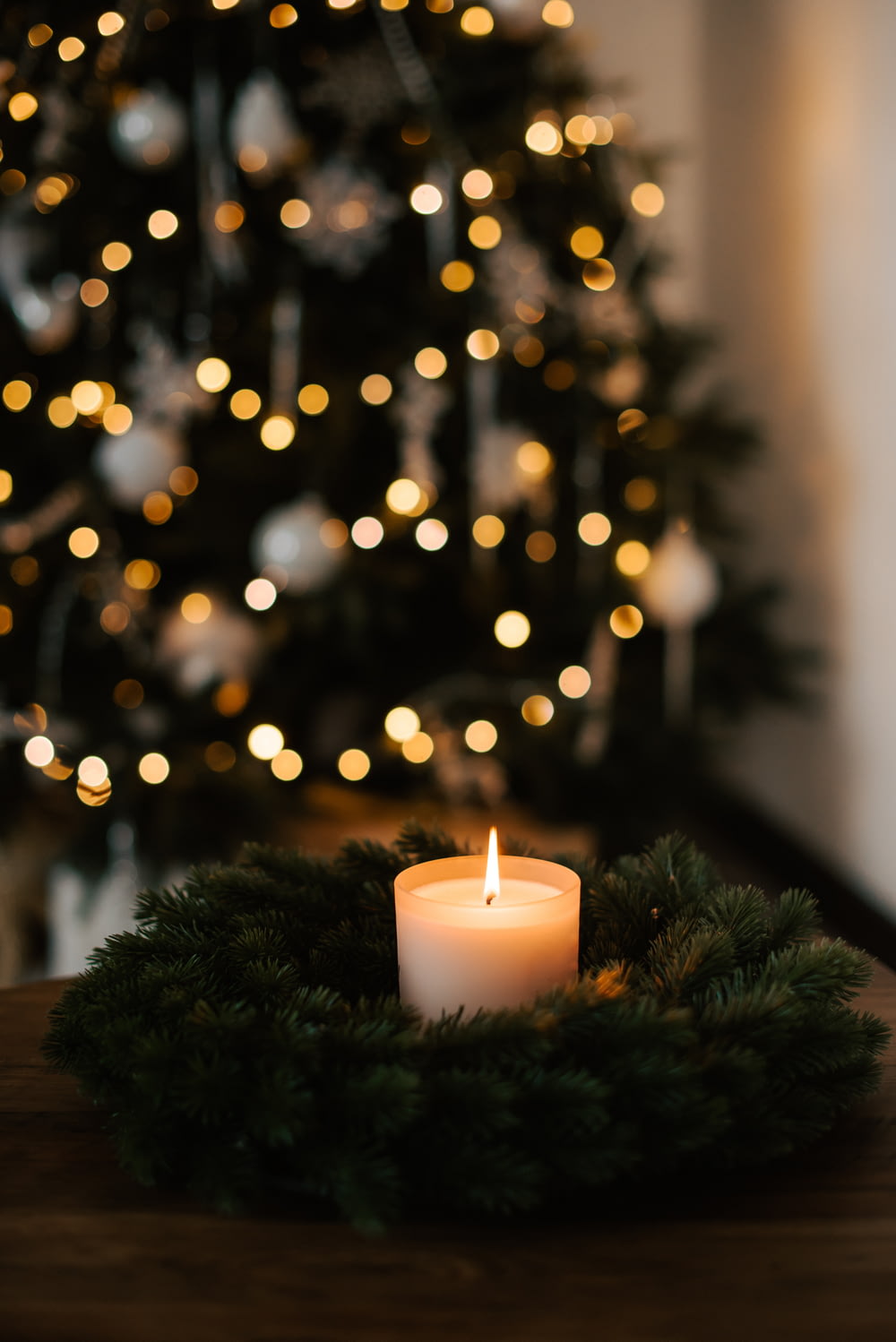 a lit candle on a table in front of a christmas tree