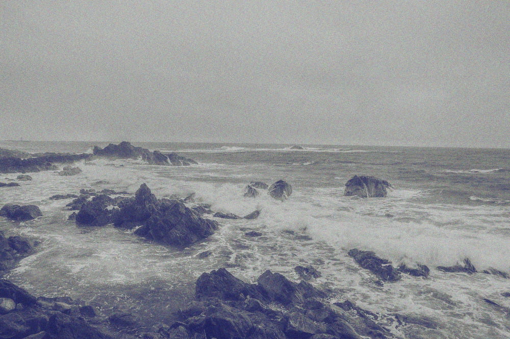 a black and white photo of waves crashing on rocks