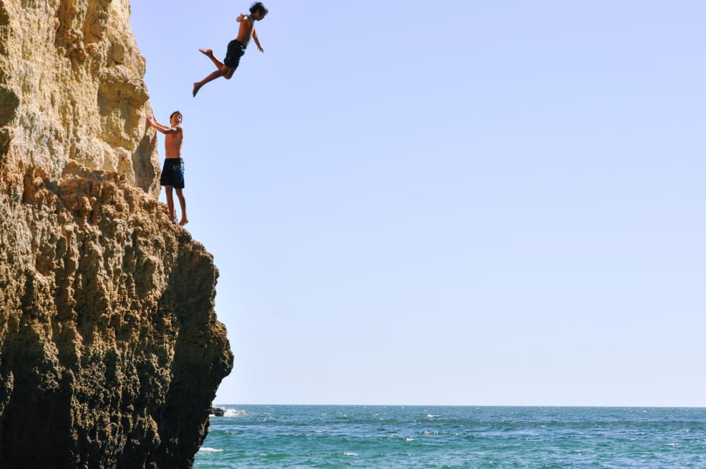 two people jumping off a cliff into the ocean
