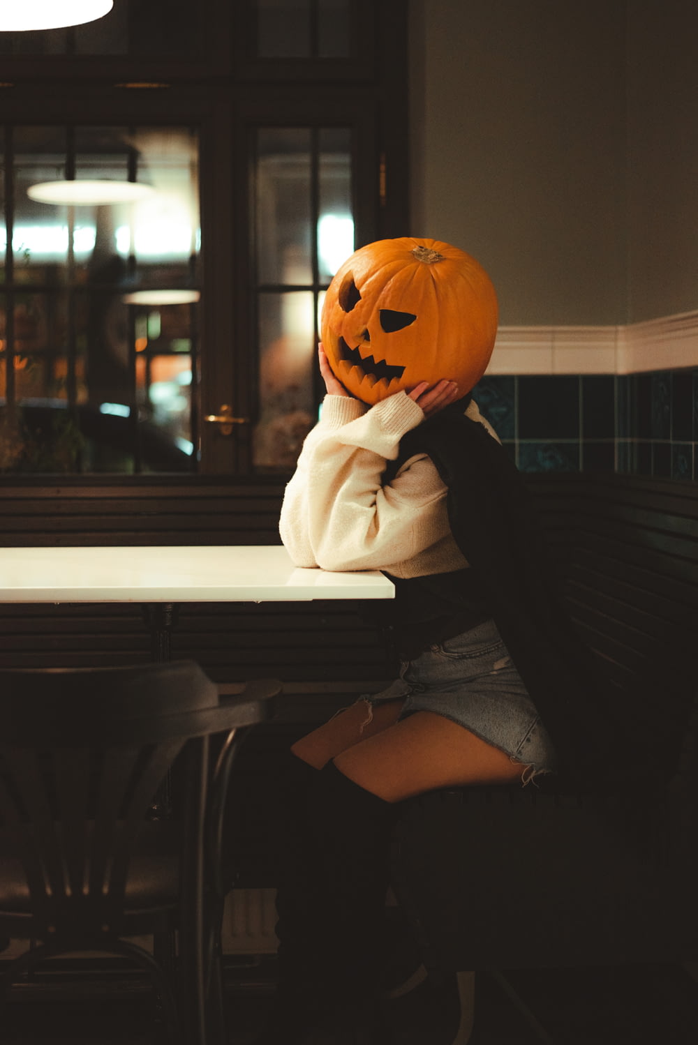 a woman sitting at a table with a pumpkin on her head