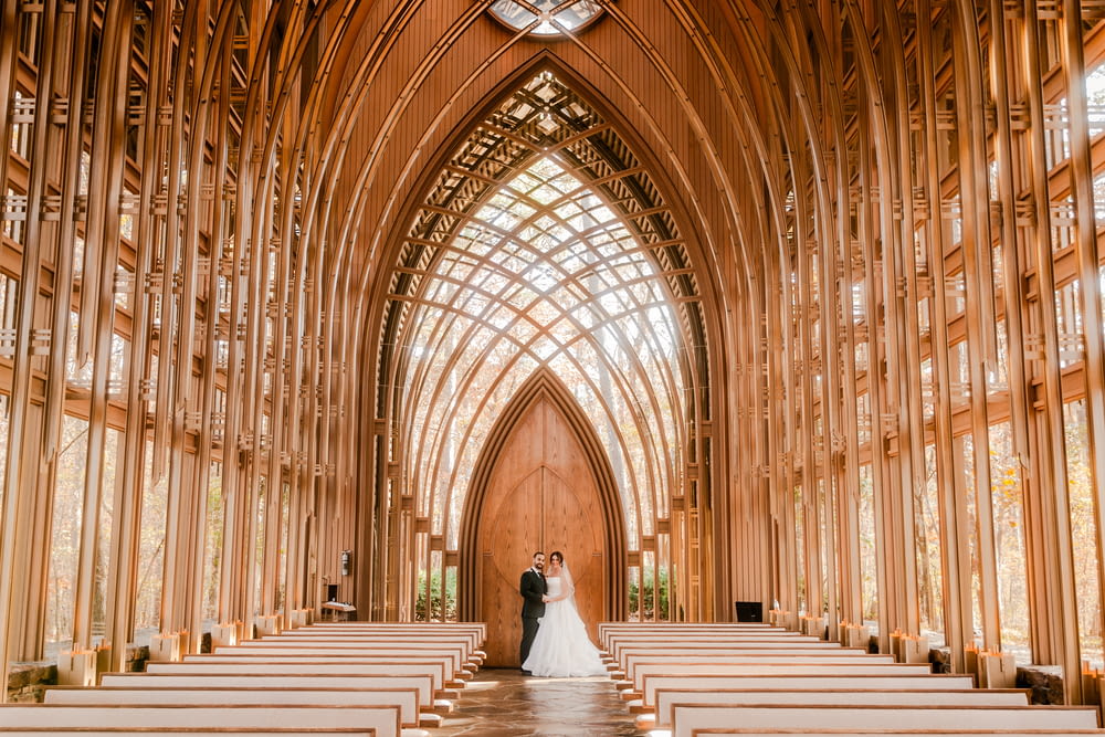 a bride and groom standing at the end of a church aisle