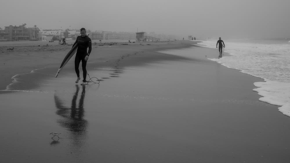 two surfers walking on the beach with their boards