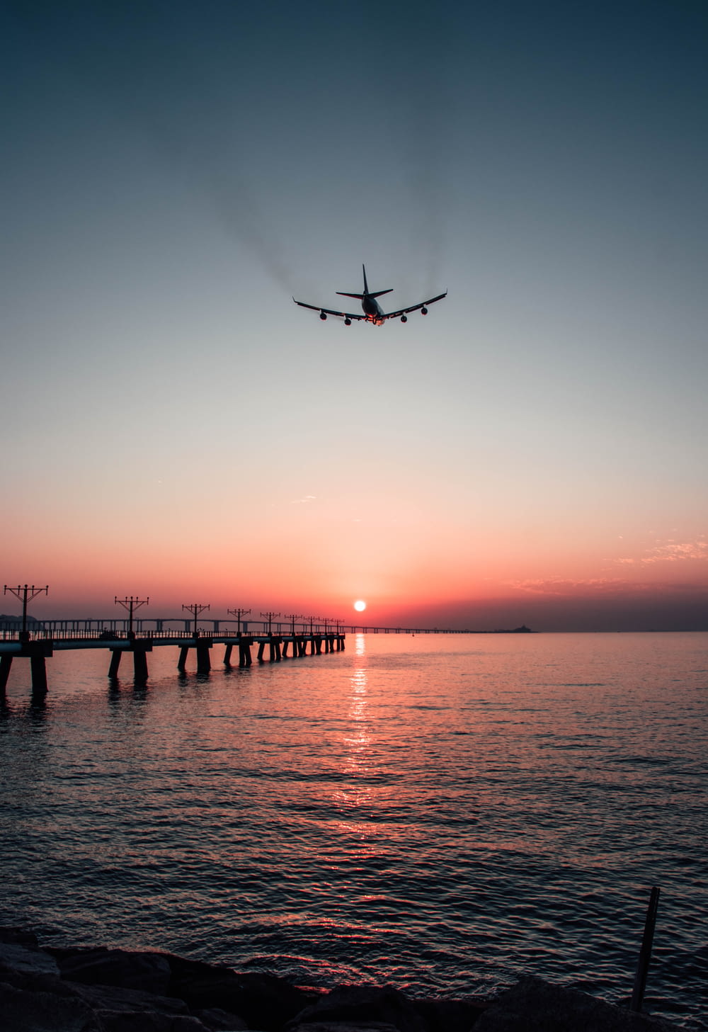 an airplane flying over a body of water at sunset