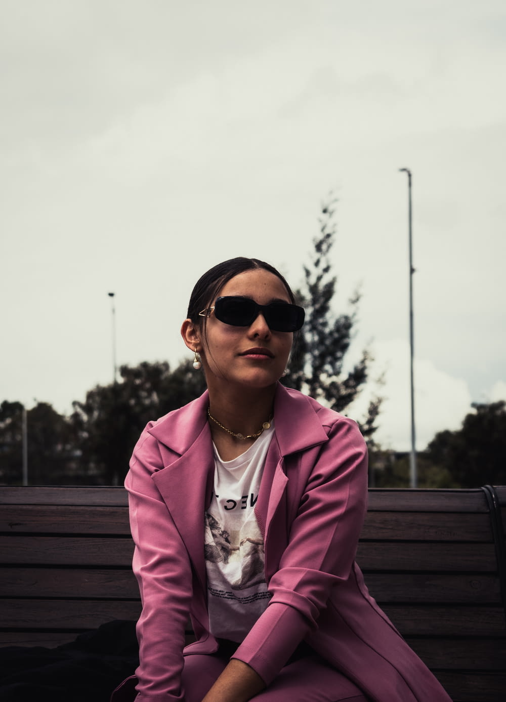 a woman in a pink coat and sunglasses sitting on a bench