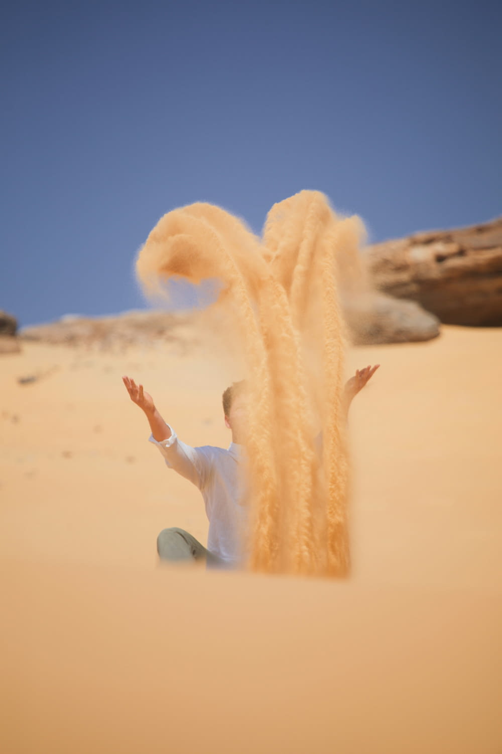 un homme assis dans le sable jetant du sable en l’air
