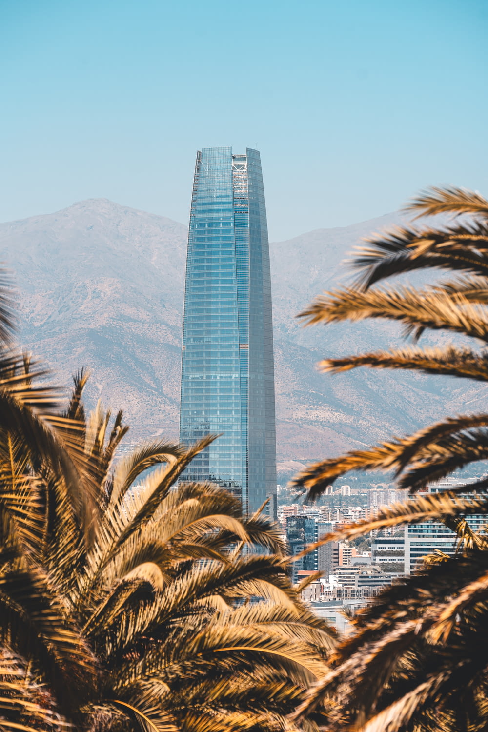 a tall building surrounded by palm trees in front of a mountain