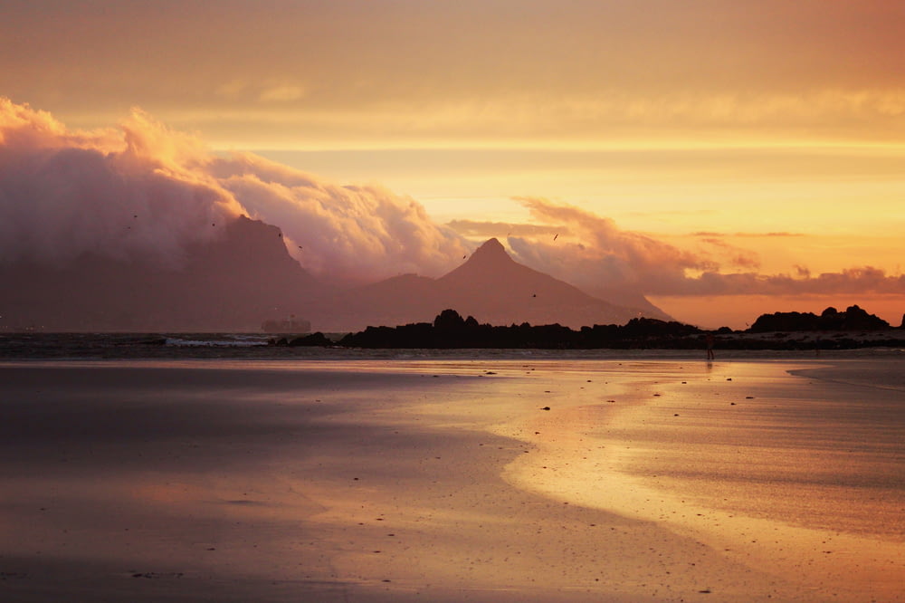 a sunset view of a beach with a mountain in the background