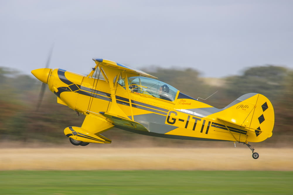 a small yellow airplane flying over a lush green field