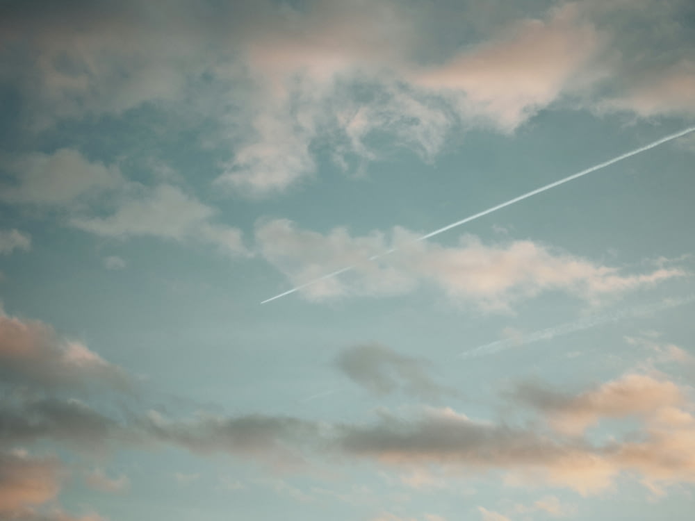 a plane flying through a cloudy sky with a contrail in the sky