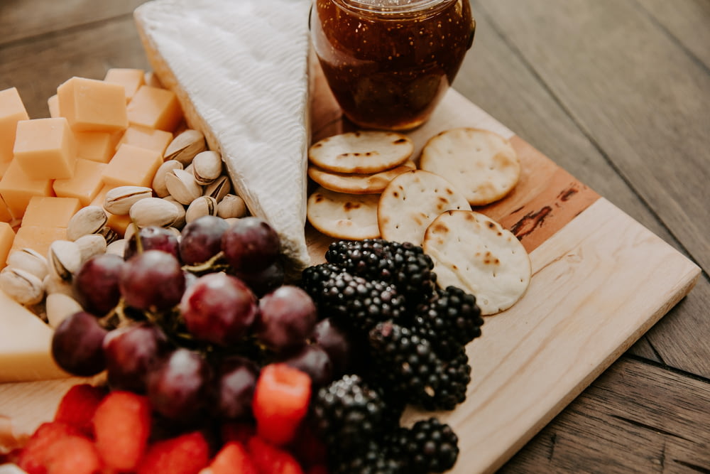 a wooden cutting board topped with cheese, fruit and crackers