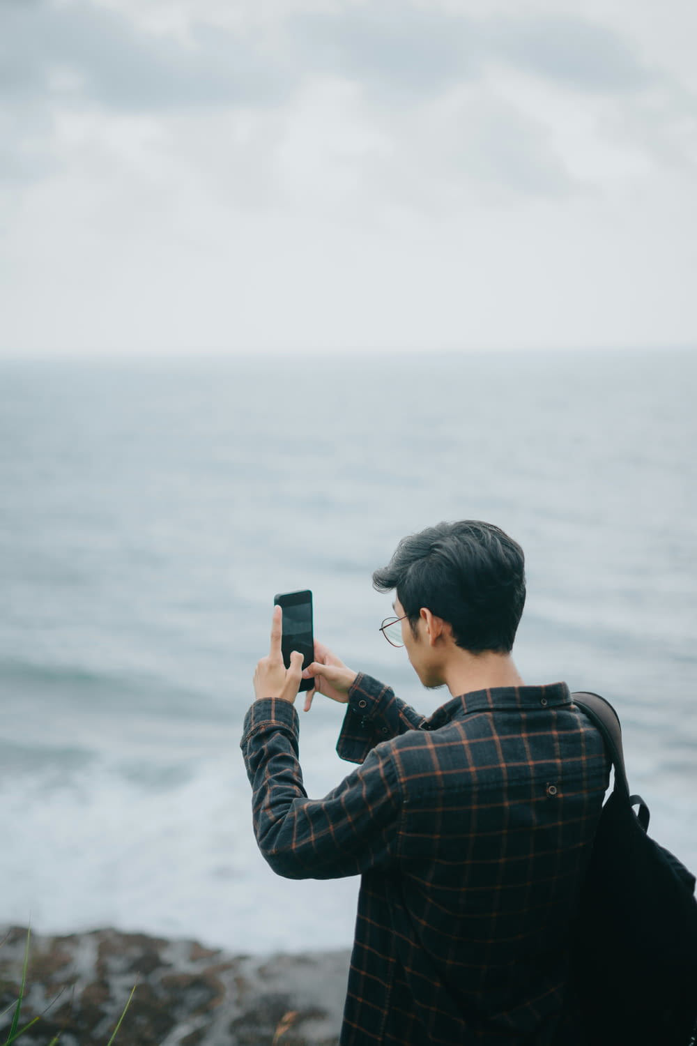 a man taking a picture of the ocean with his cell phone