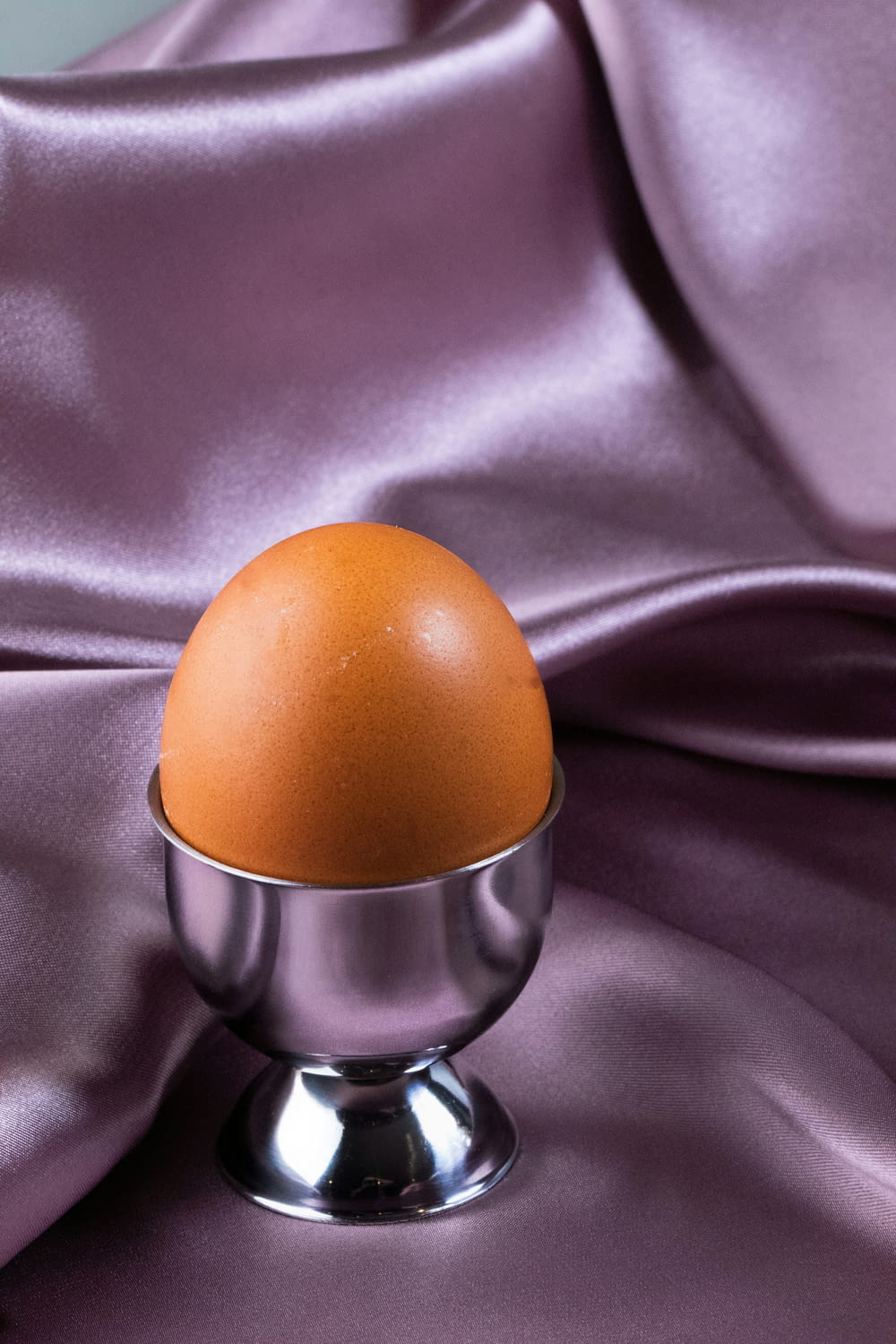 an egg in a silver bowl on a purple satin