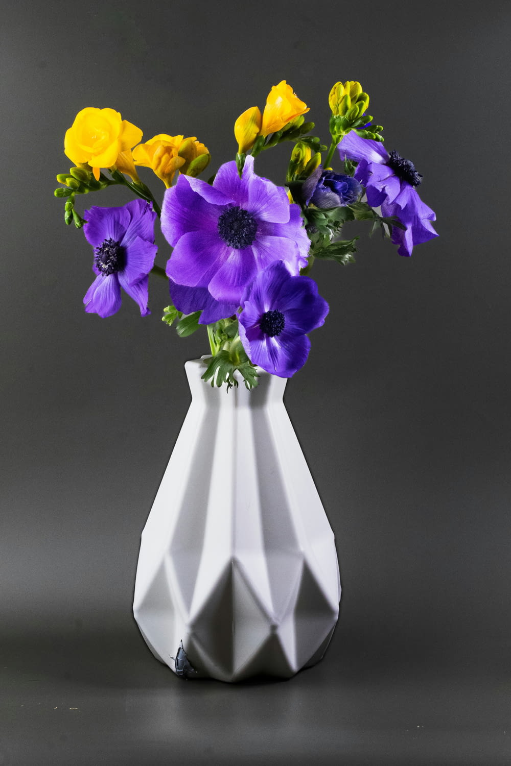 a white vase filled with purple and yellow flowers