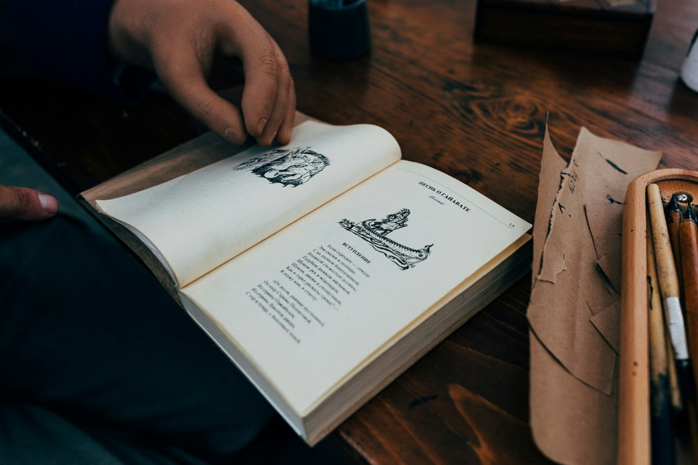 uma pessoa segurando um livro aberto em cima de uma mesa de madeira