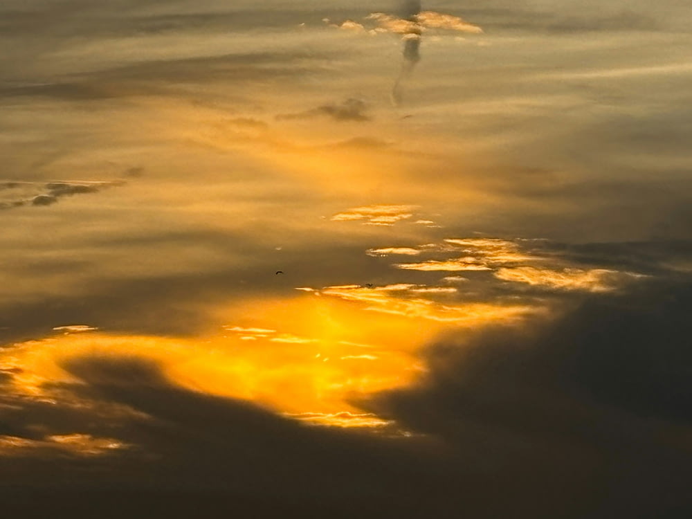 a plane flying through a cloudy sky at sunset