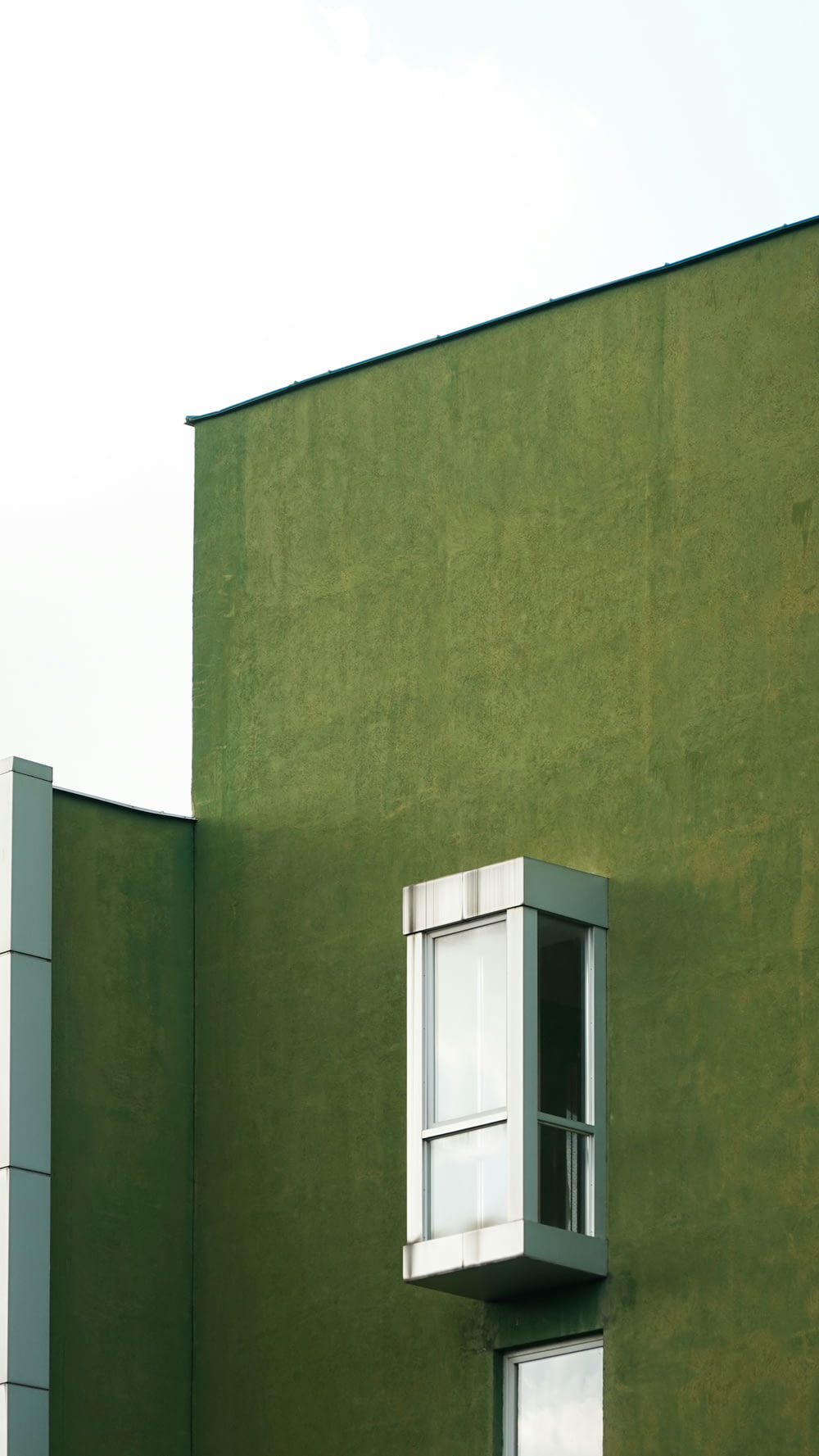 a tall green building with a window and a sky background