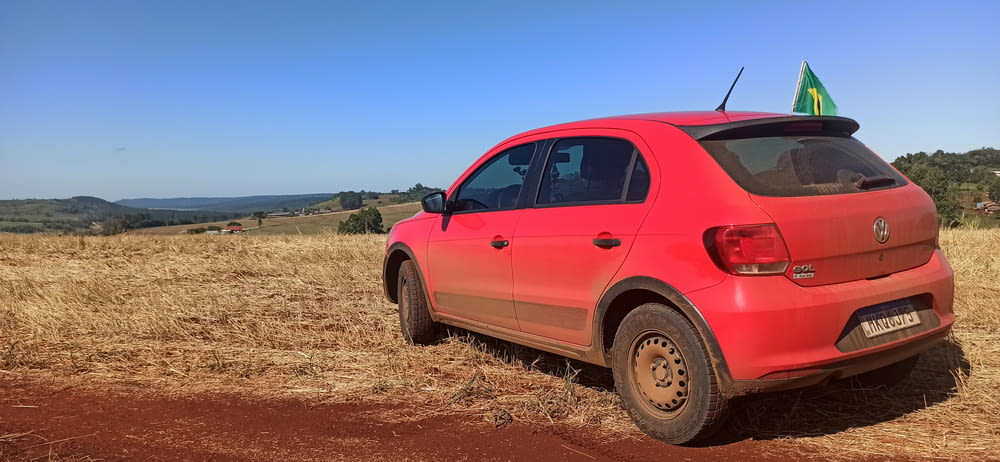 a red car parked in a field of dry grass