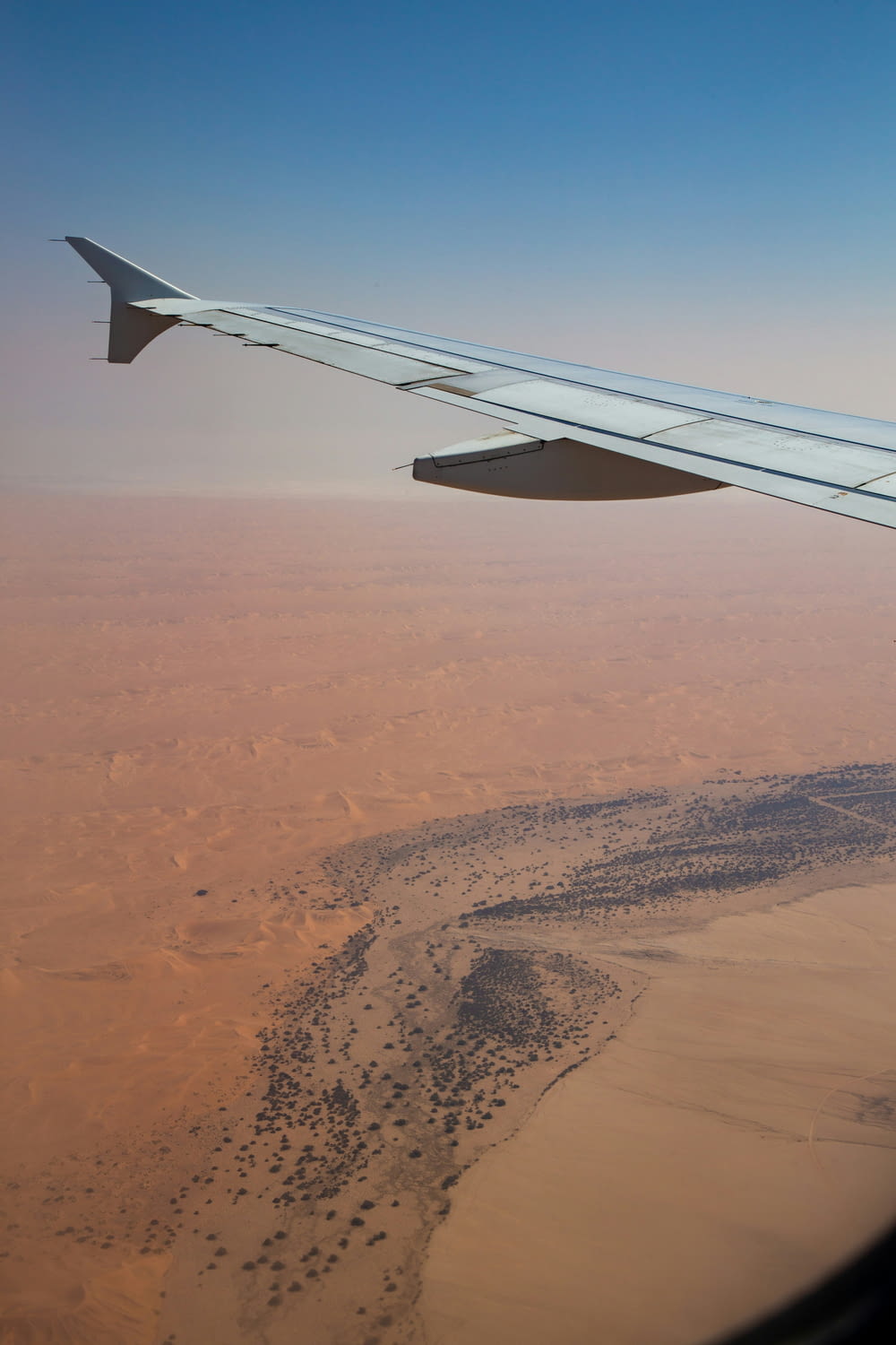 el ala de un avión volando sobre un desierto