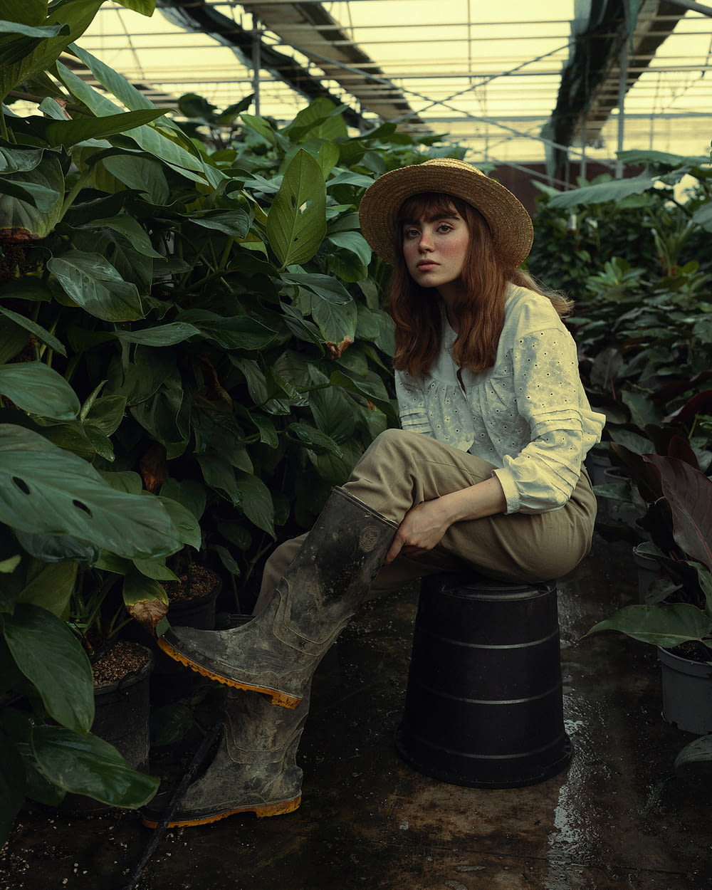 a woman sitting on a barrel in a greenhouse